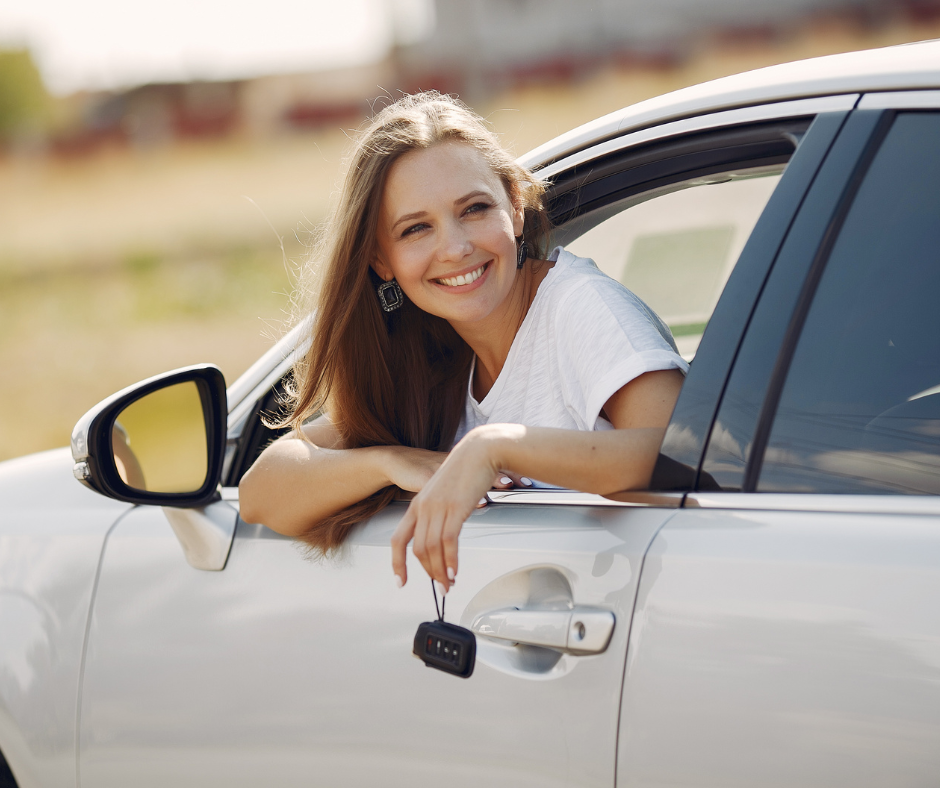 A young woman leaning out of the window of a car, showcasing how to save money when you drive.